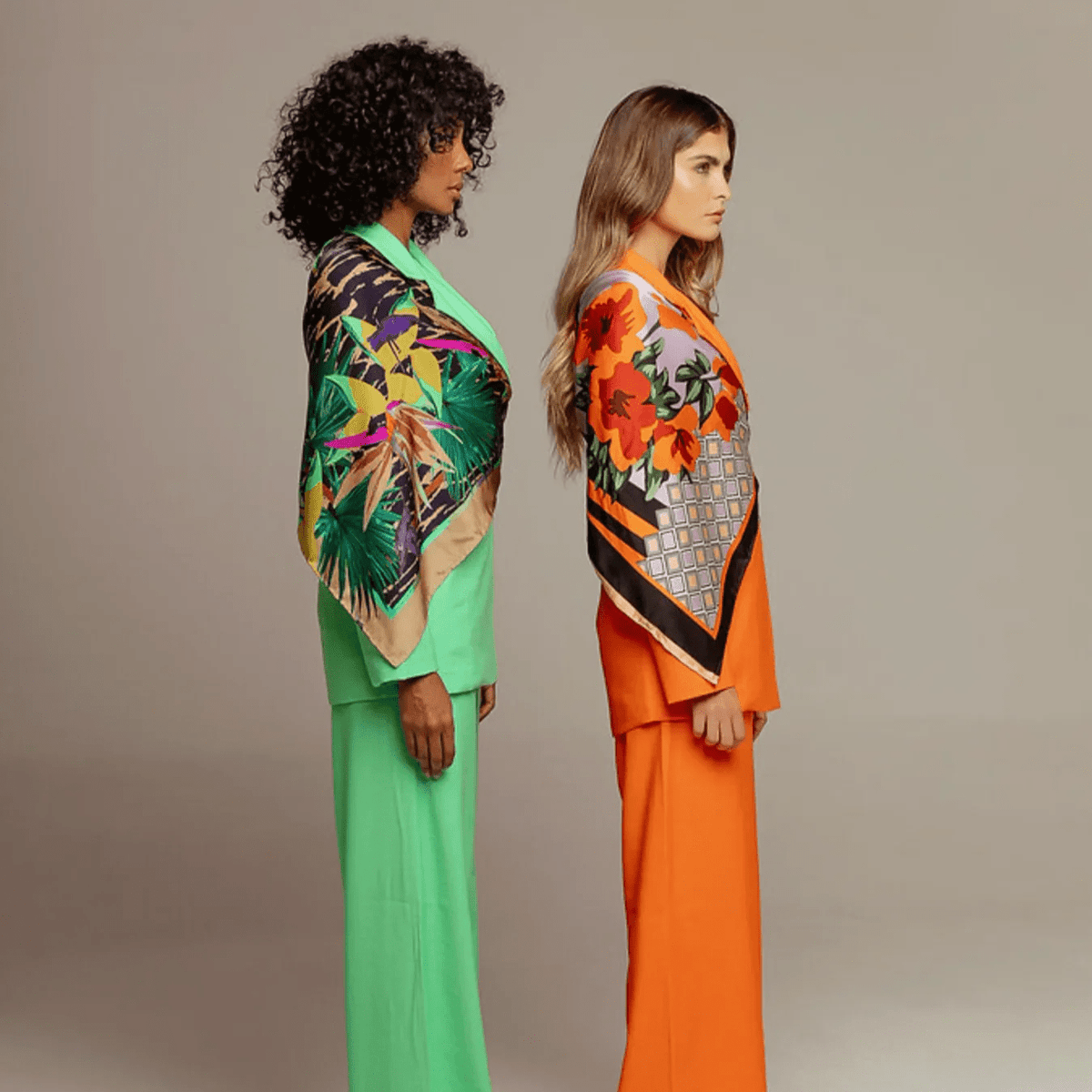 Two women in vibrant green and orange outfits with bold print scarves, sustainable fashion