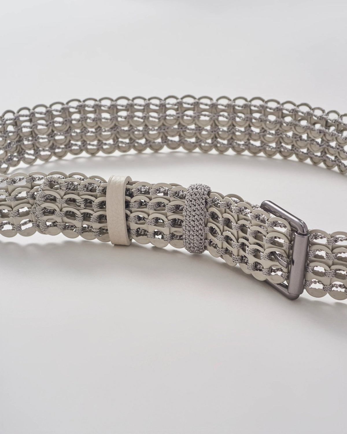 Handcrafted beige woven belt with circular metal details and silver buckle on white background