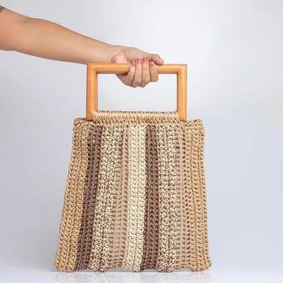 Hand holding striped crochet handbag with wooden rectangular handles against white background