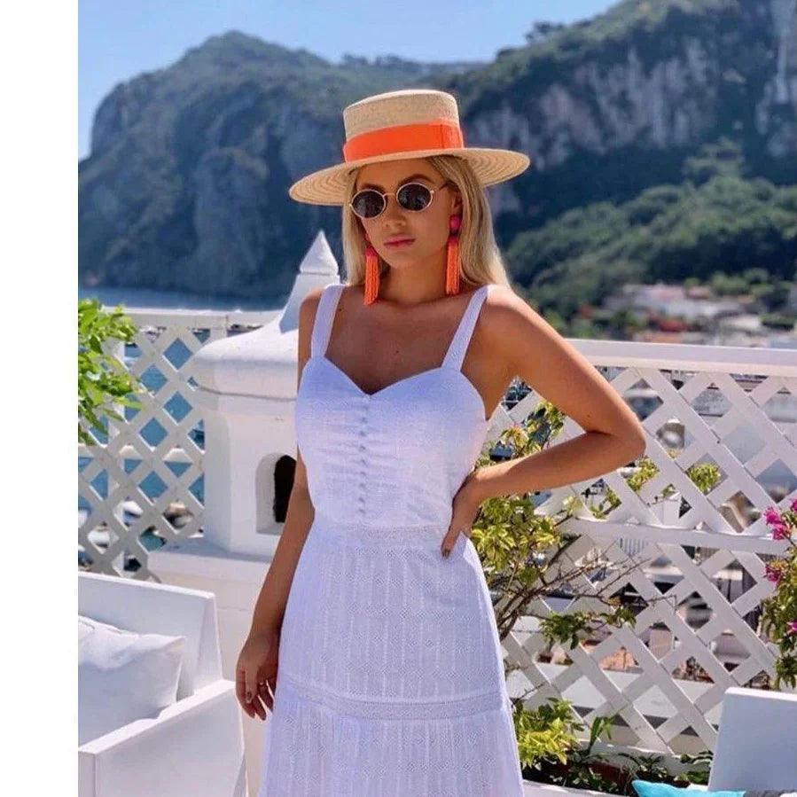 Woman wearing a large brim straw boater hat with orange band, white sundress, and sunglasses outdoors