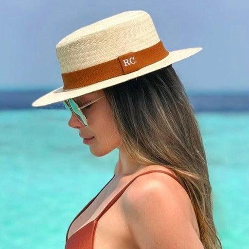 Woman wearing a carnauba straw boater hat with brown band by the ocean, beach fashion