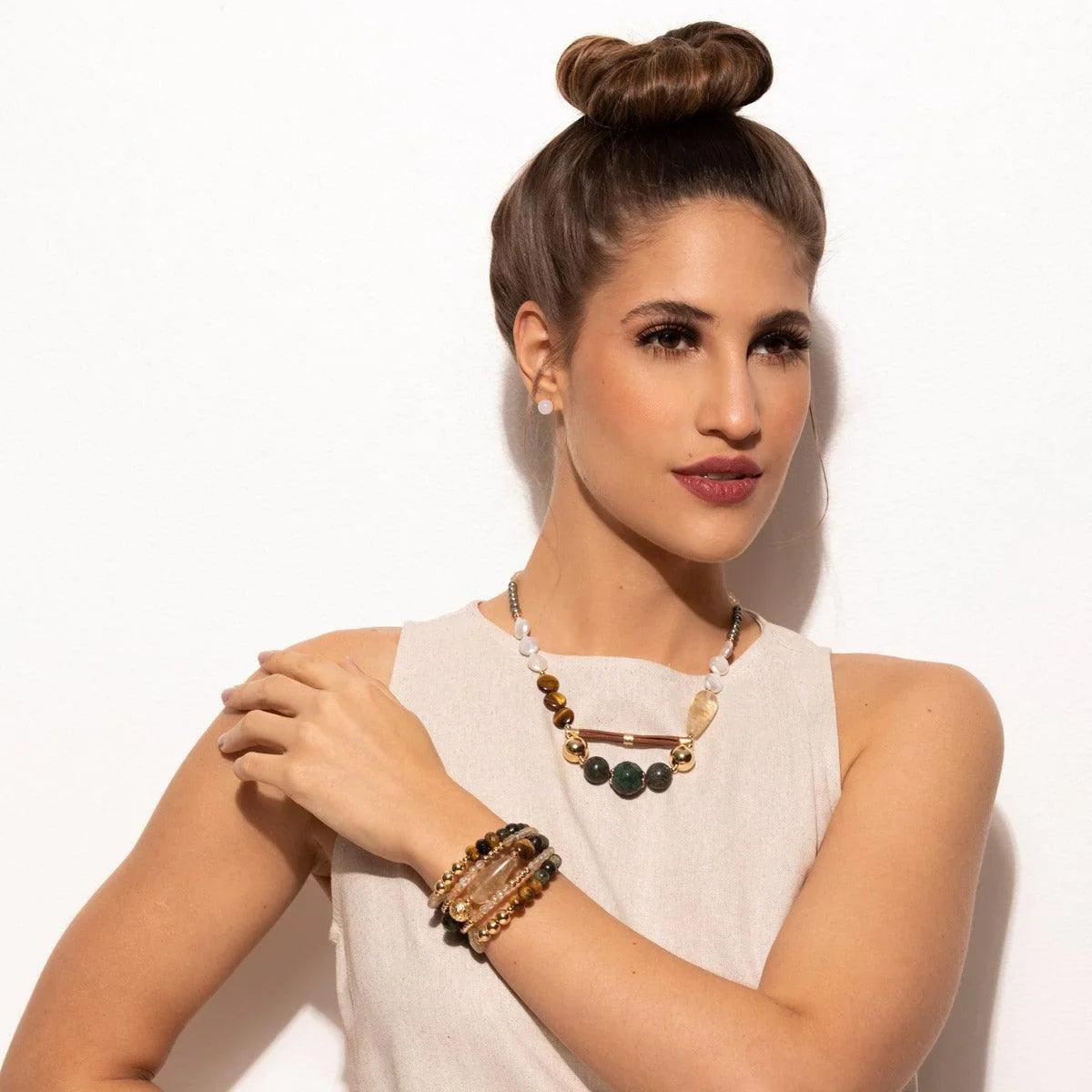 Woman wearing layered onyx beads bracelet and gemstone necklace in neutral outfit