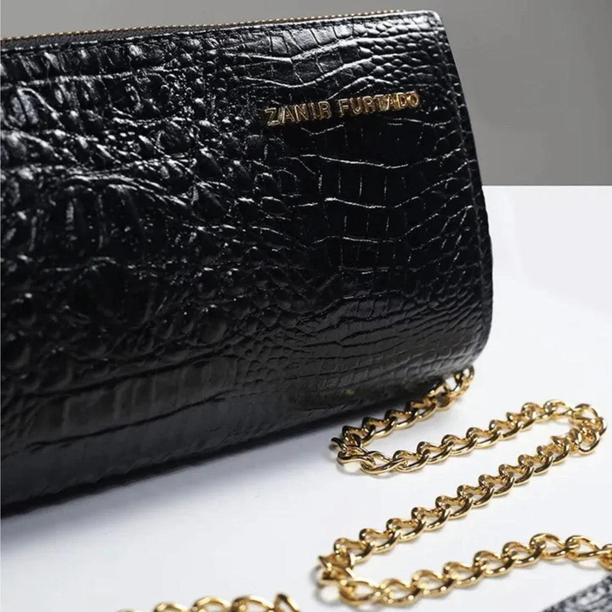 Black textured clutch bag with gold logo detail and gold chain strap on white surface
